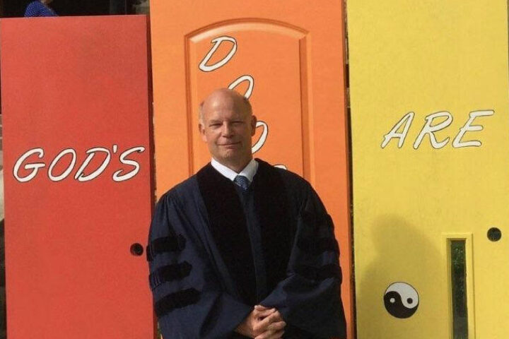 The Rev. Dr. Bob Livingston stands in front of doors painted the colors of the rainbow. They read, "God's doors are open to all."