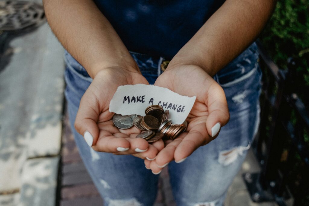 Cupped hands hold coins and a small slip of paper saying 'Make a Change.'