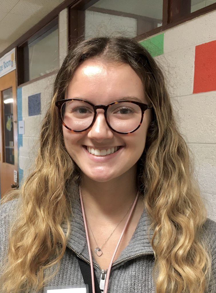 A smiling young woman with glasses and long dark blonde hair.