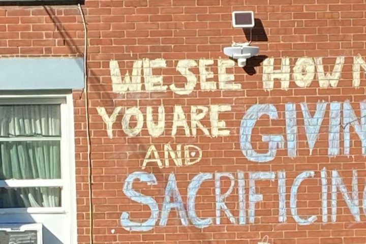 Image of a brick wall with graffiti reading 'We see how much you are giving and sacrificing.'