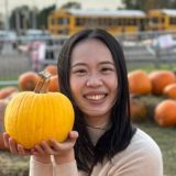 Photo of Yi-Hui, a smiling Taiwanese young woman, sitting in a pumpkin patch and holding a pumpkin.