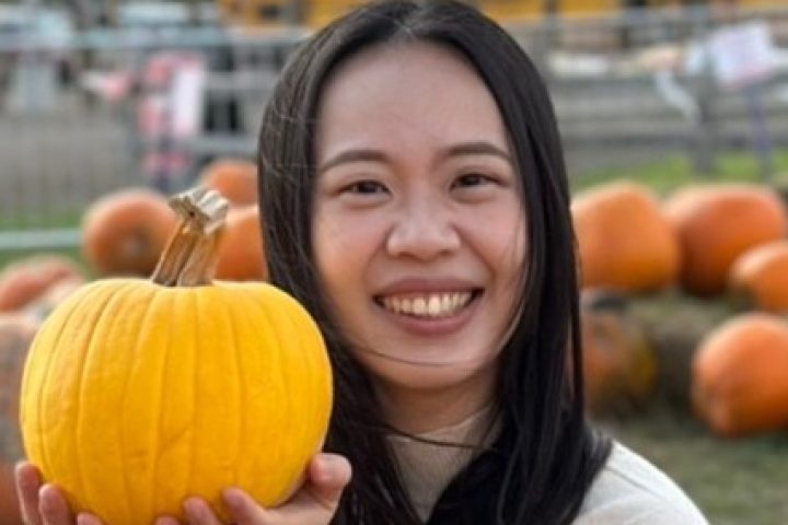 Photo of Yi-Hui, a smiling Taiwanese young woman, sitting in a pumpkin patch and holding a pumpkin.